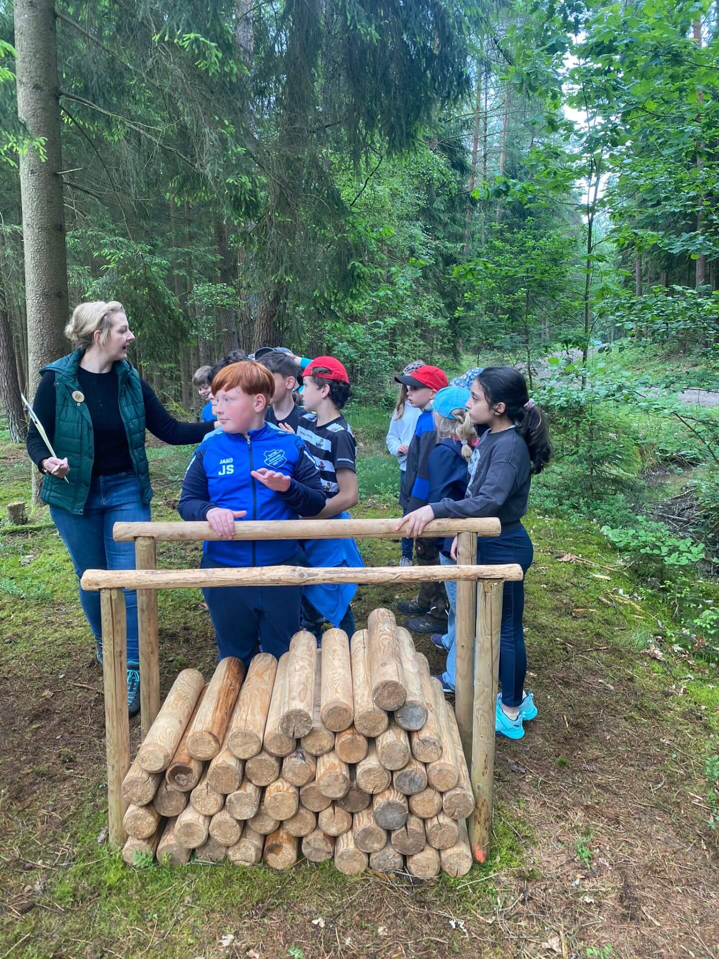 Kinder warten auf Spielbeginn bei Holzstoß im Wald