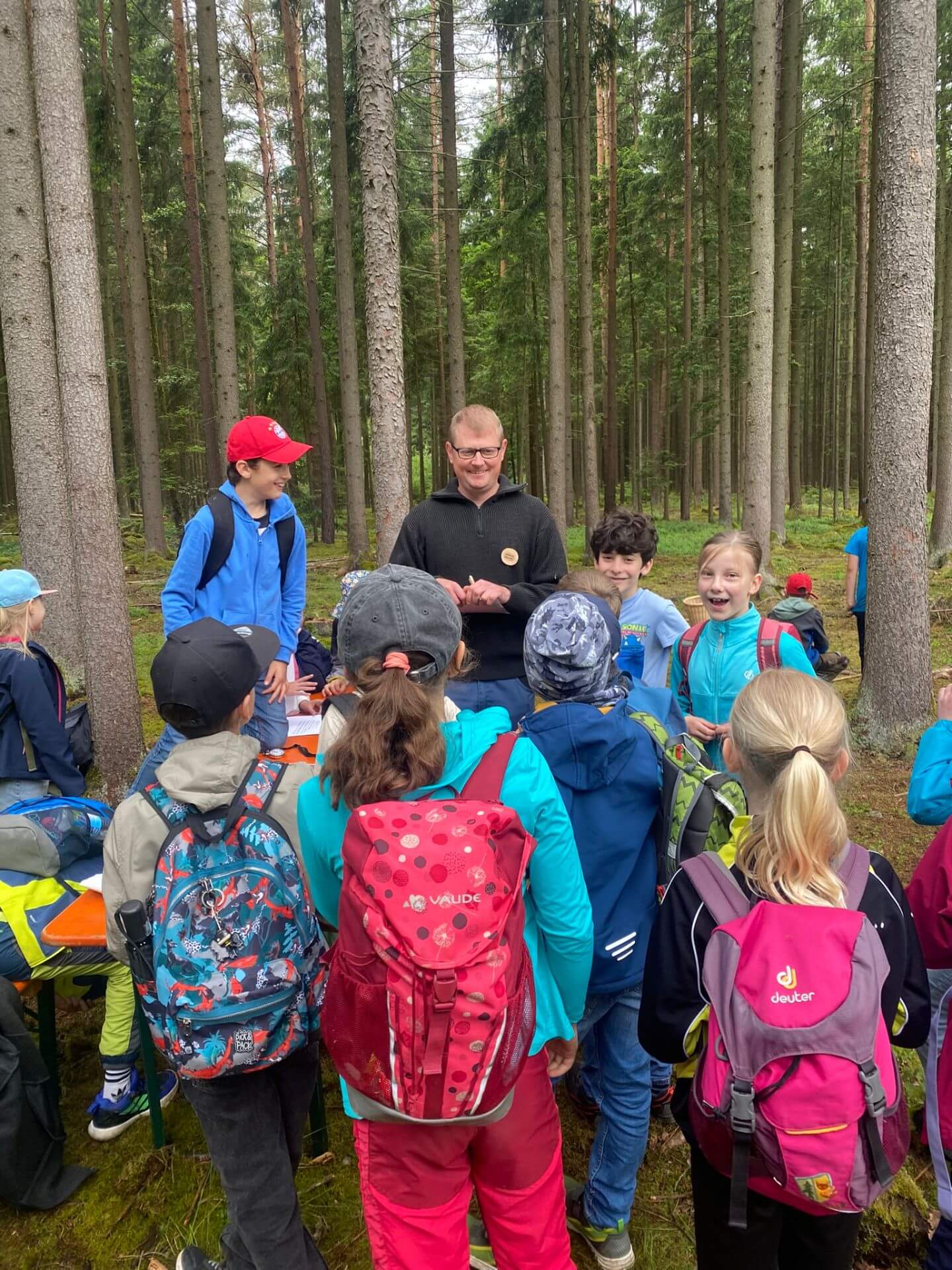 Förster steht lachend mit Klasse im Wald