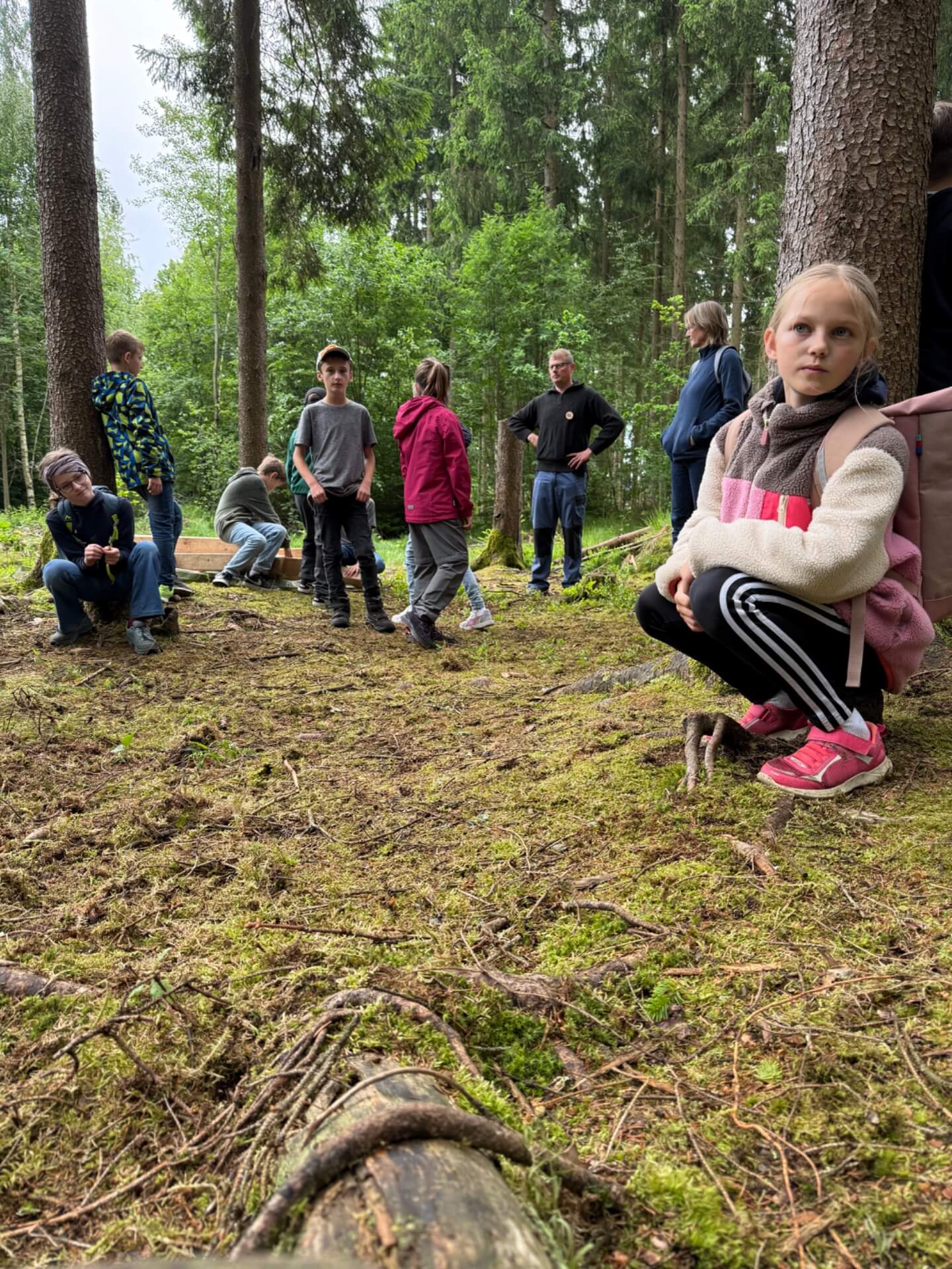 Mädchen kniet vor Baum weitere Schüler im Hintergrund